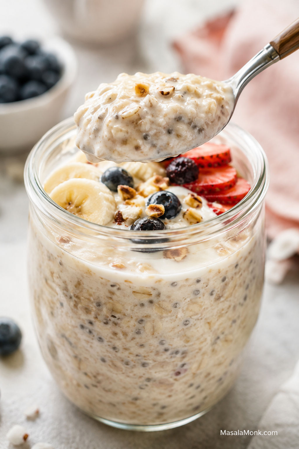 Creamy overnight oats in a glass jar with fresh fruit, nuts, and a spoon lifting a thick bite.
