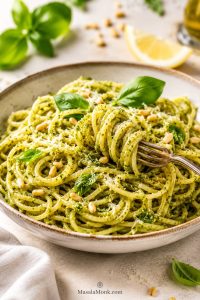 Bowl of glossy pesto pasta with basil leaves, Parmesan, pine nuts and a lightly sauced green coating