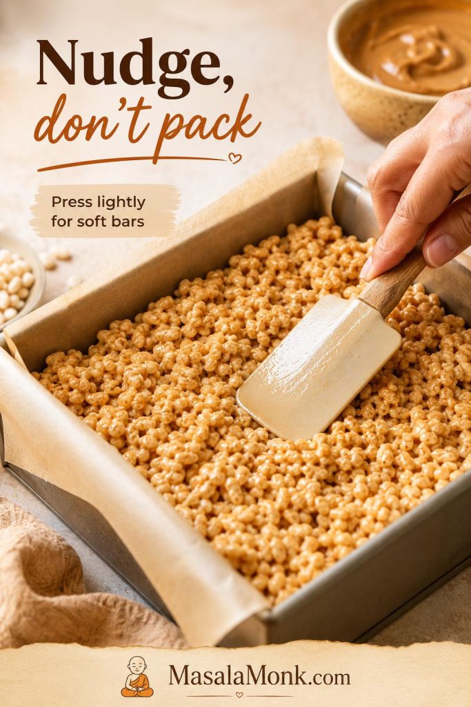 Peanut butter rice crispy treat mixture being pressed lightly into a parchment-lined pan with a spatula.
