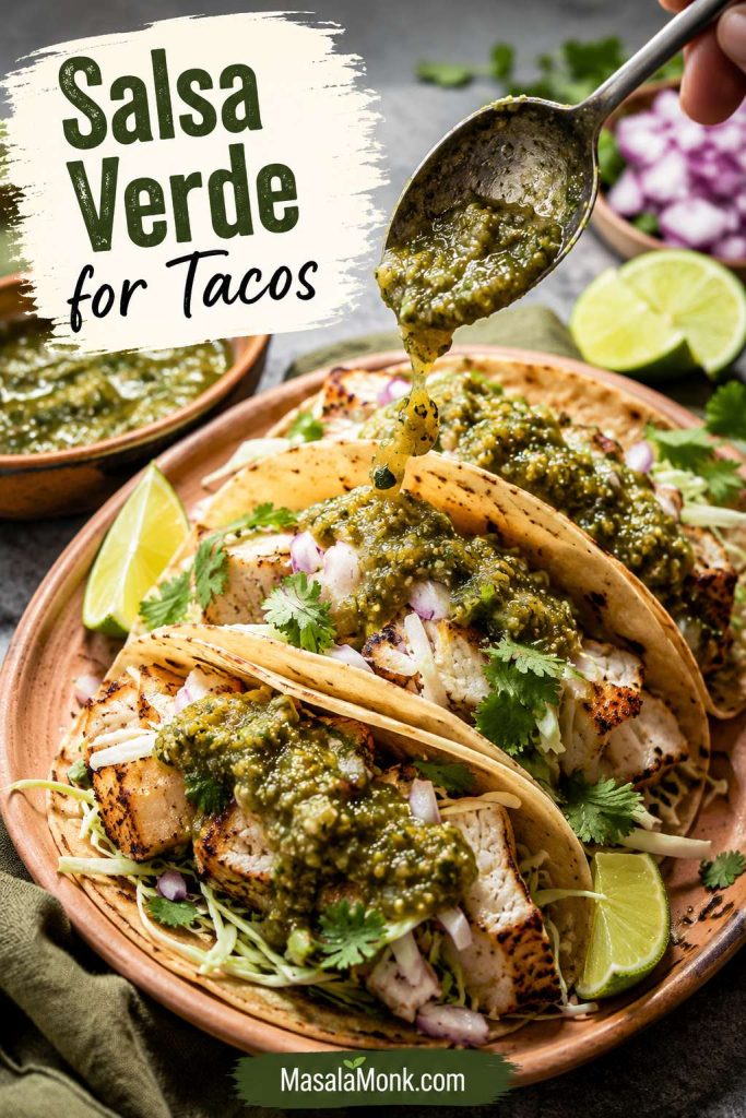 Salsa verde being spooned over tacos with lime, cilantro, onion, and warm tortillas