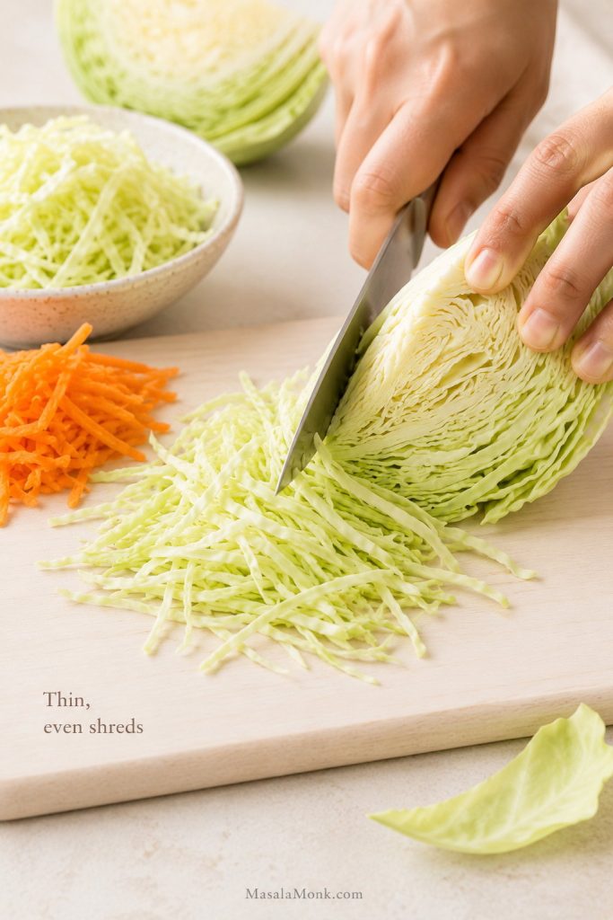 Hands slicing green cabbage into thin shreds on a cutting board for homemade coleslaw.
