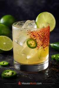 Spicy margarita on the rocks with a half Tajín rim, lime garnish, jalapeño slice, clear ice, and condensation on the glass.