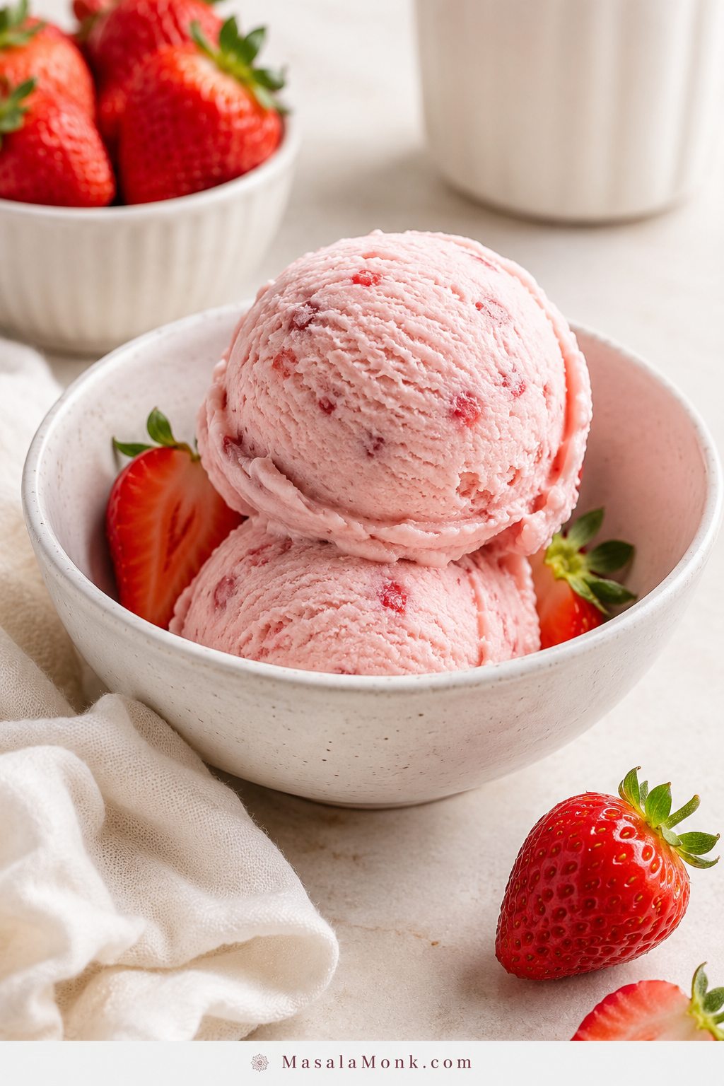 Homemade strawberry ice cream scooped into a pale bowl with fresh strawberries nearby