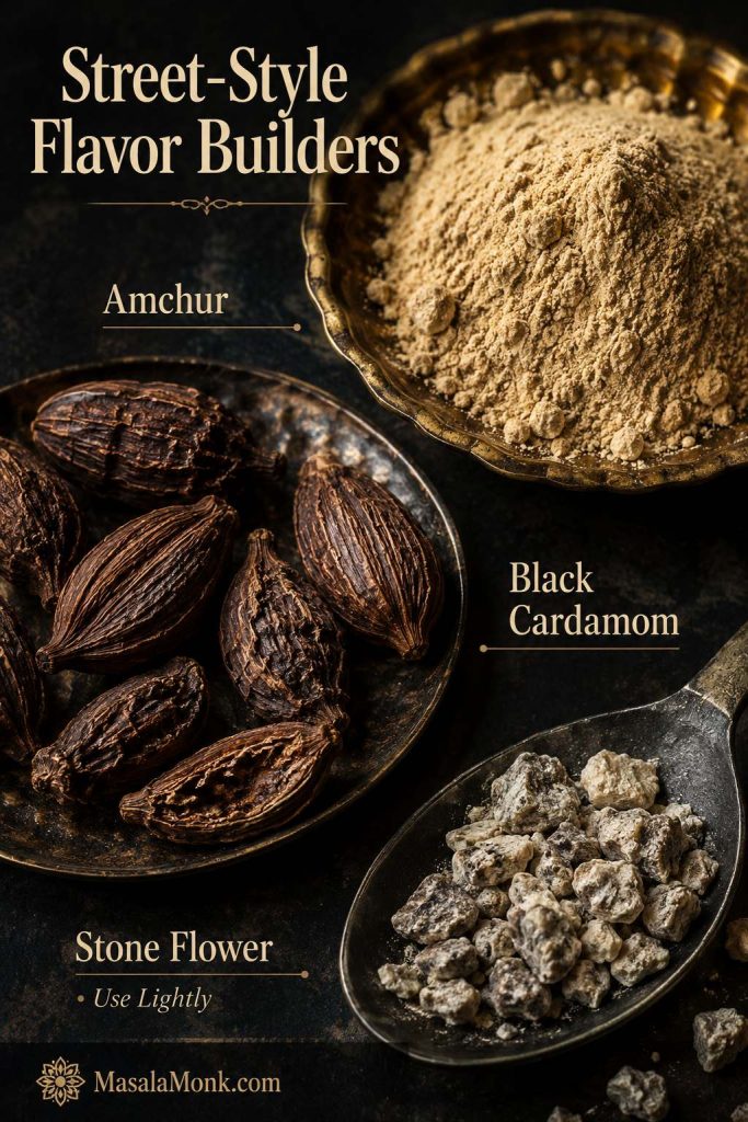 Close-up of amchur powder, black cardamom pods, and a small pinch of stone flower for street-style pav bhaji masala flavor.