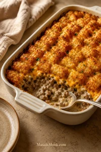 Tater tot casserole with golden crispy tots, creamy ground beef filling, cheddar, and a scoop served from a 9x13 dish