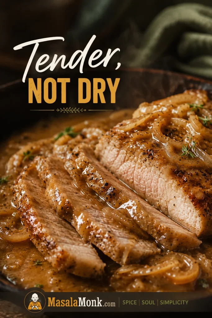 Sliced smothered pork chop with a moist interior, glossy onion gravy, and soft cooked onions on the plate.