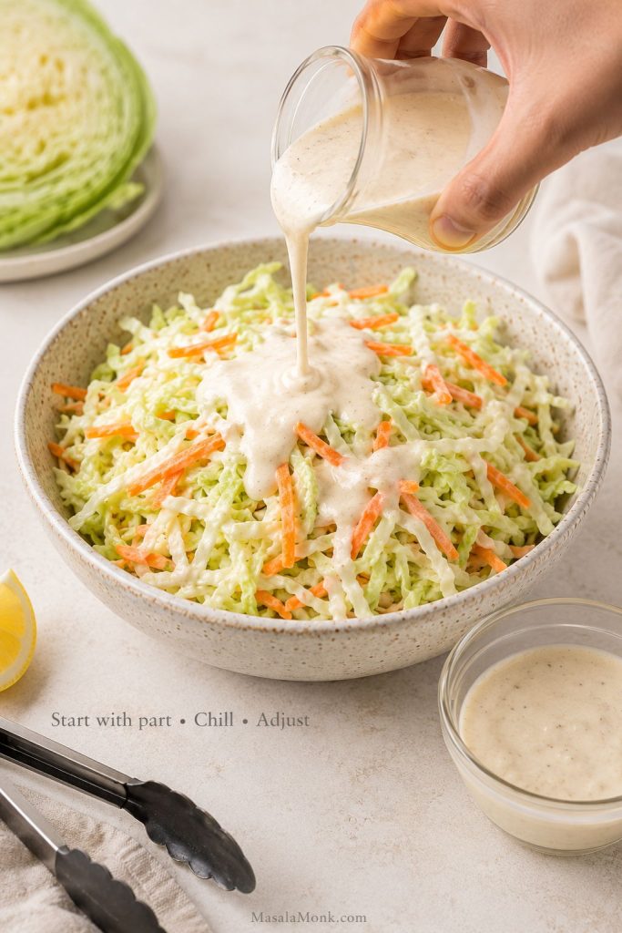 Creamy dressing being poured over shredded cabbage with extra reserved dressing in a small bowl beside it.