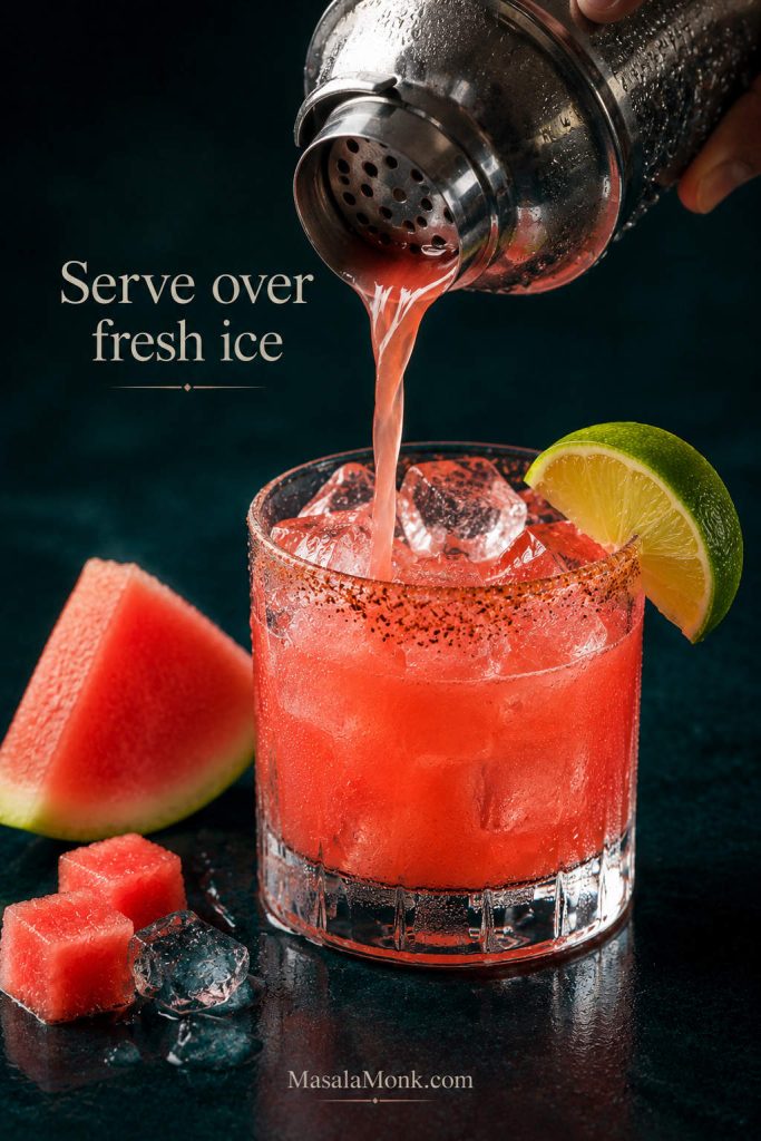 Watermelon margarita being poured from a shaker into a glass filled with fresh ice.
