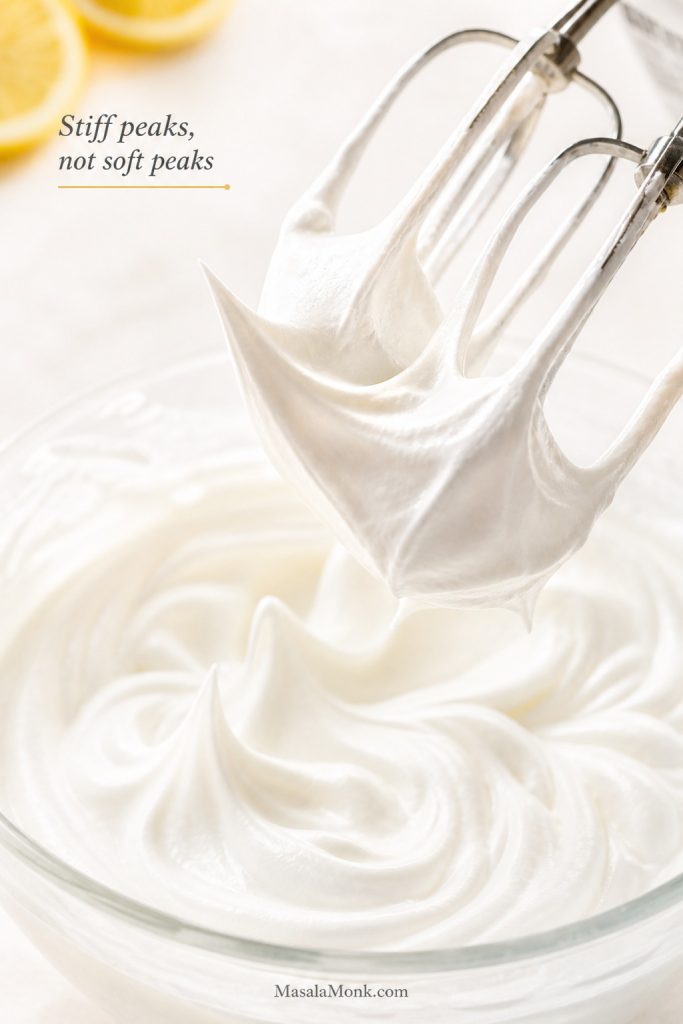 Mixer beaters lifting whipped cream into stiff peaks in a bowl