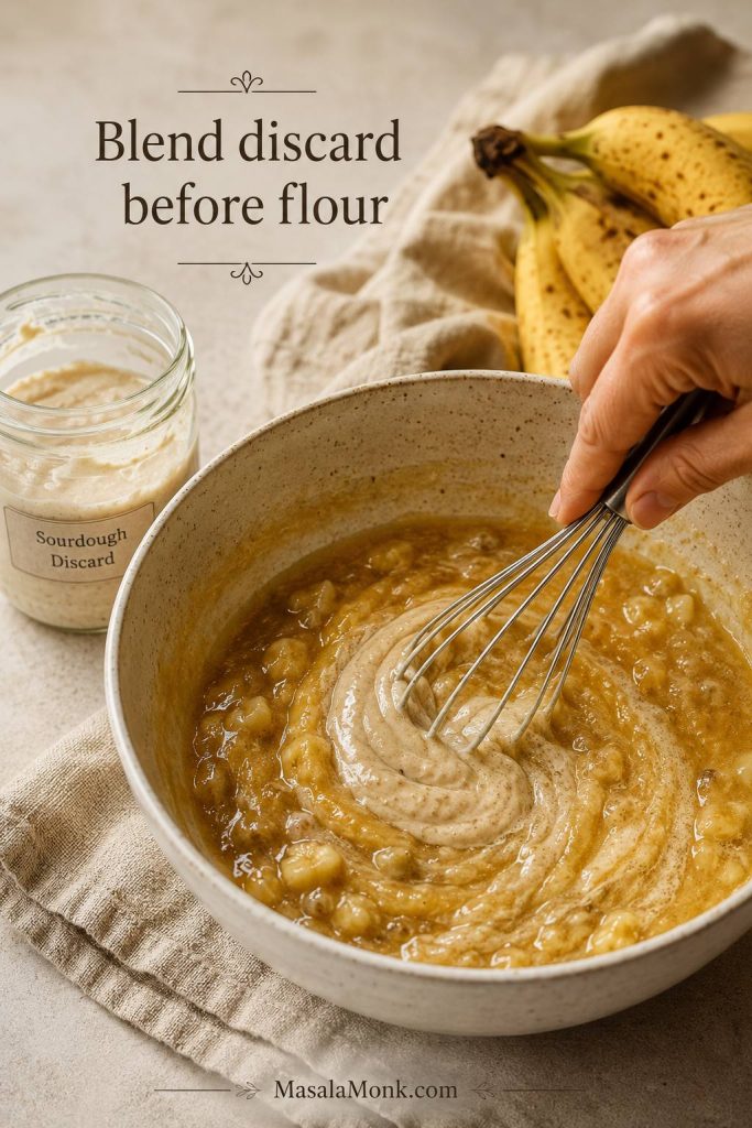 Hand whisking sourdough discard into banana bread wet ingredients in a bowl before flour is added.