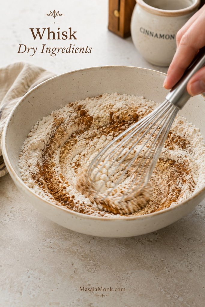 Flour, baking powder, baking soda, salt, and warm spices being whisked together in a bowl for applesauce cake.