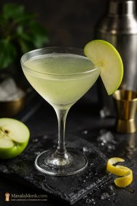 Pale green Appletini in a chilled coupe glass with a thin green apple slice garnish on a dark bar surface.