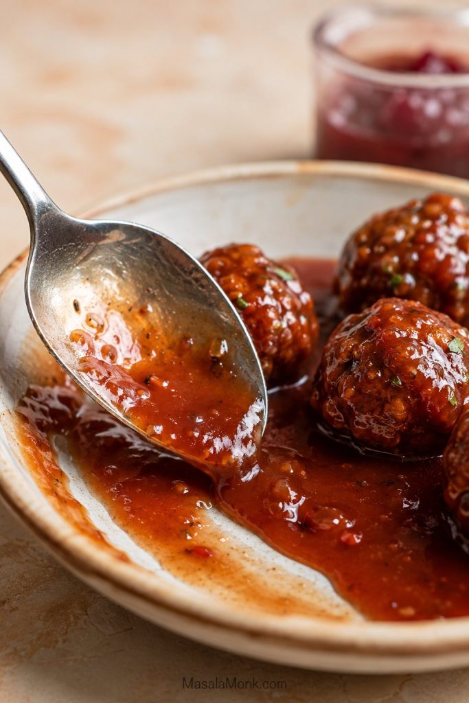 Spoon dragging through grape jelly meatball sauce to show sauce that is thick enough to cling but still pourable.