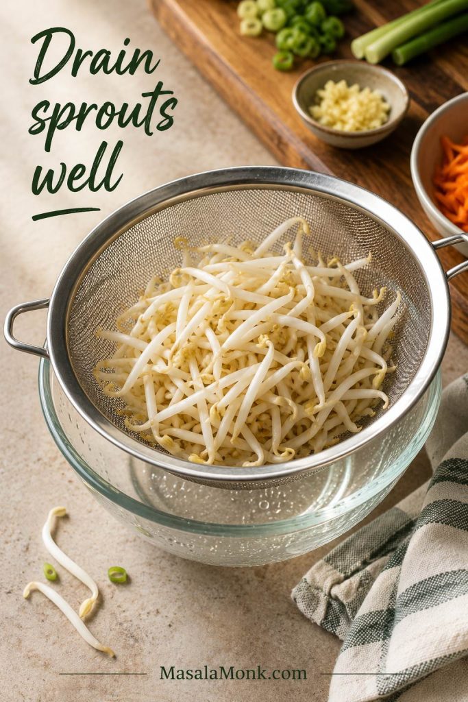 Fresh bean sprouts draining in a fine mesh strainer over a bowl on a kitchen counter.