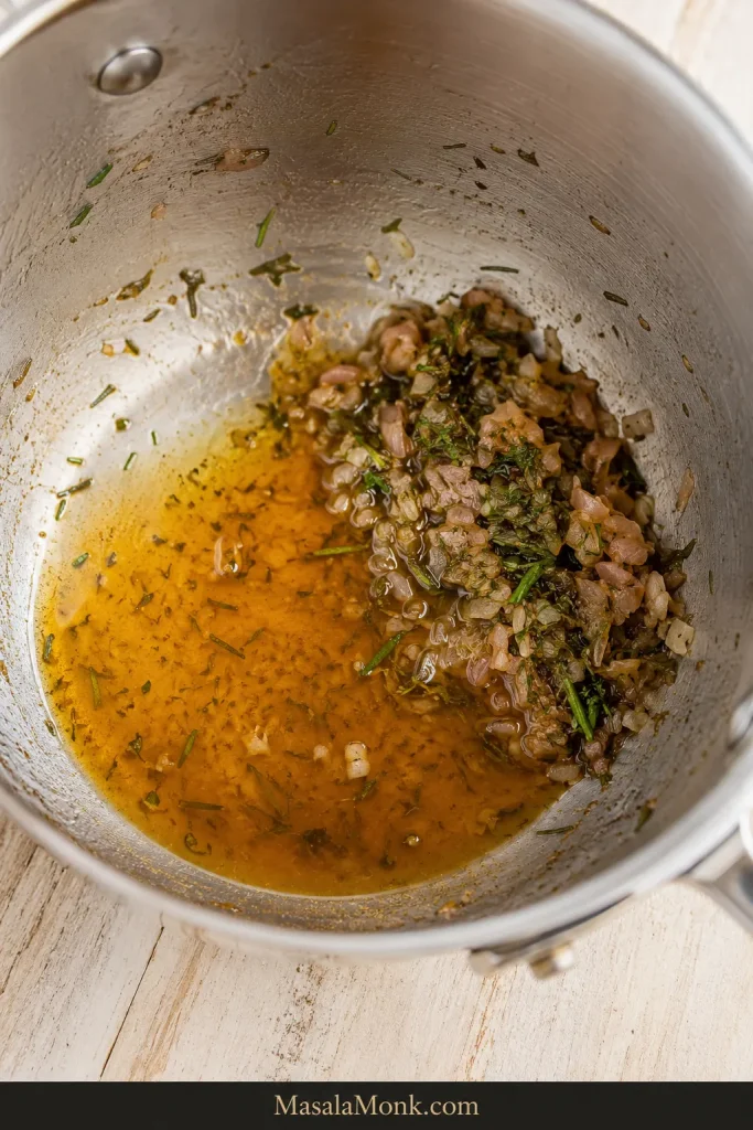 Small glossy puddle of concentrated tarragon reduction left in a saucepan with shallots and herbs pushed to one side.