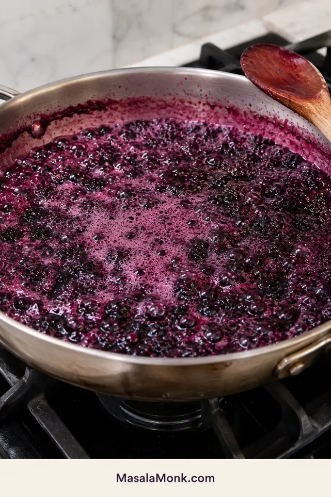 Blackberry jam bubbling loosely and foaming in a wide pan during the early cooking stage.