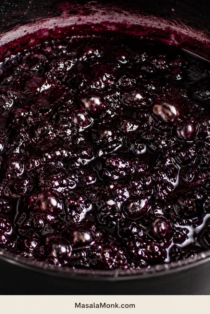 Close-up of dark glossy blackberry jam bubbles near the setting point in a pan.