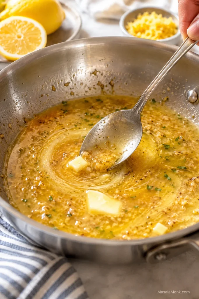 Butter melting into garlic lemon pan juices in a skillet.