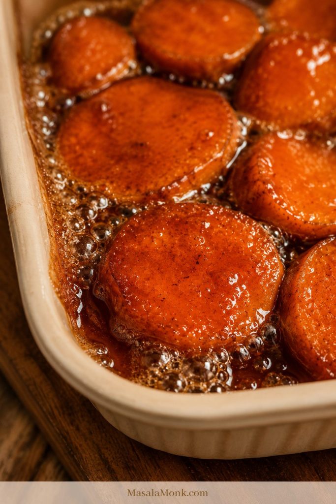 Candied yams bubbling uncovered in a cream baking dish as the sauce reduces around the orange slices.