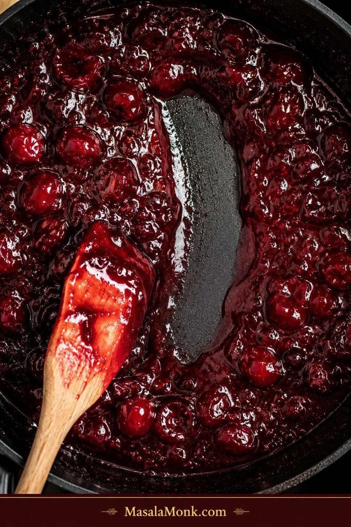 Spoon pulled through thick cherry jam in a dark pan, leaving a clear trail through the jam.