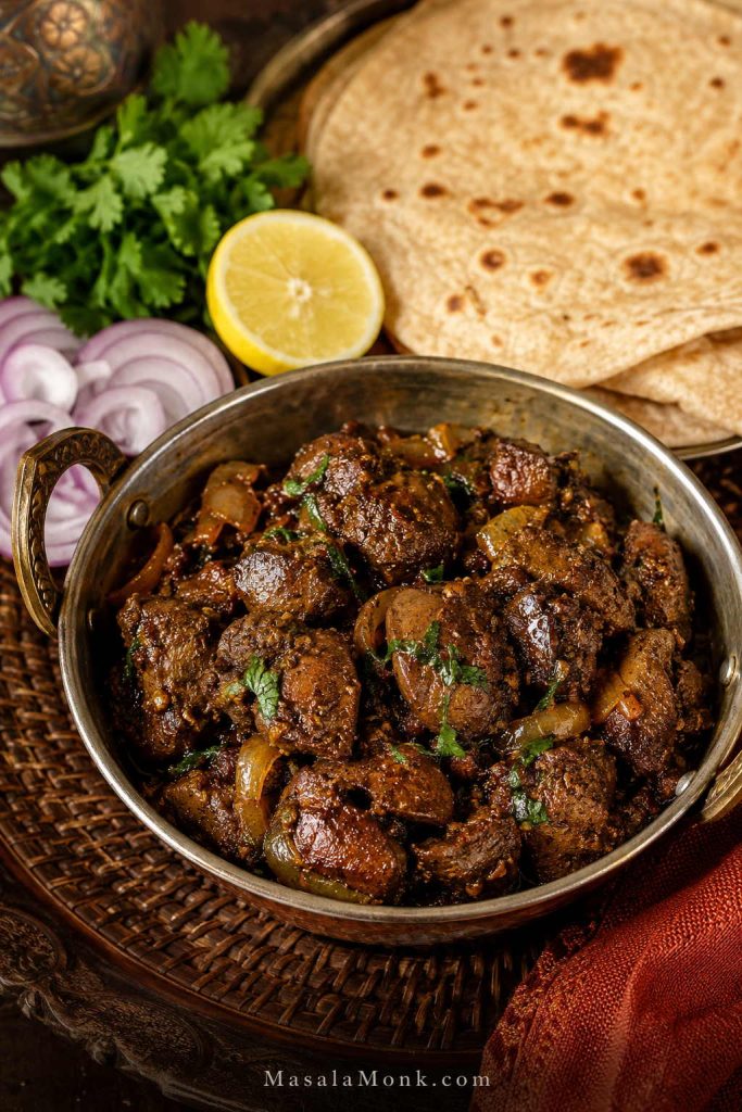 Chicken kaleji-style masala with onions served in a small pan beside roti, lemon, coriander, and sliced onions.