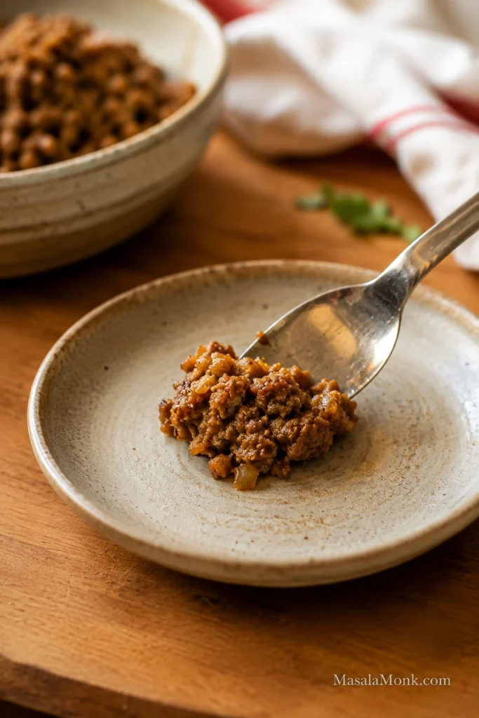 Small cooked spoonful of sausage roll filling on a plate with a bowl of filling in the background.