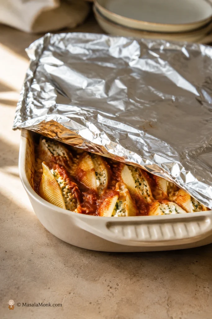 Stuffed shells in a baking dish loosely covered with foil before baking.