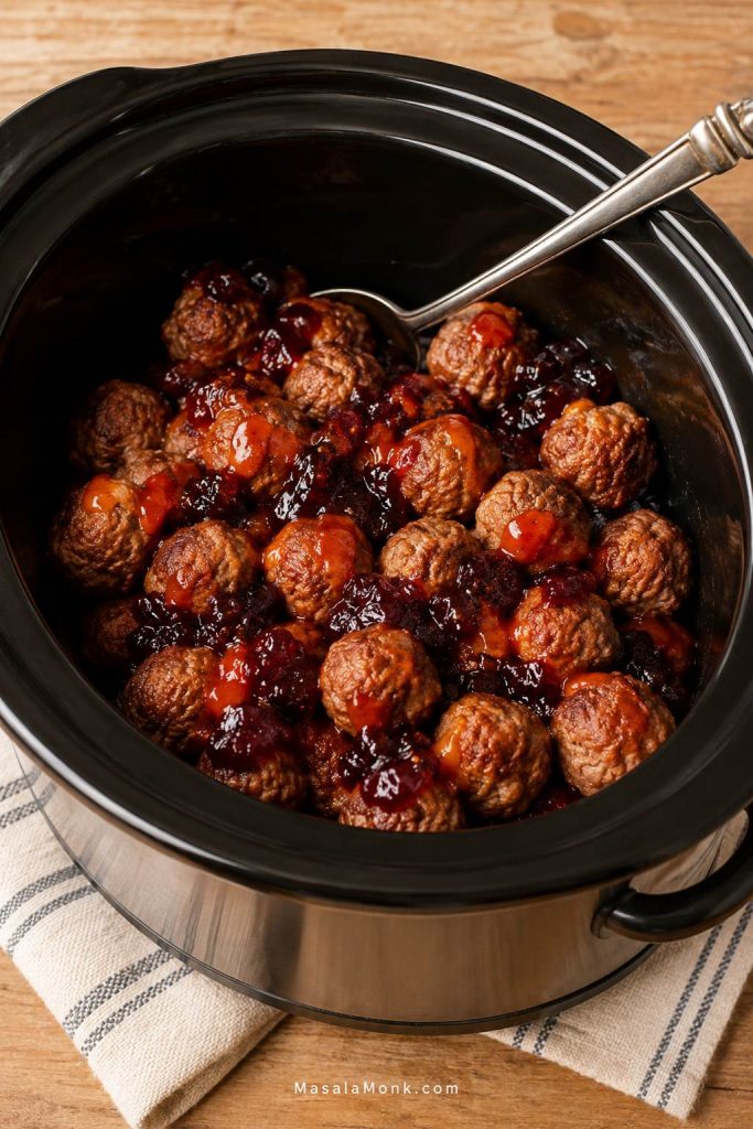 Cooked meatballs in a slow cooker with grape jelly and chili sauce before the sauce has melted together.