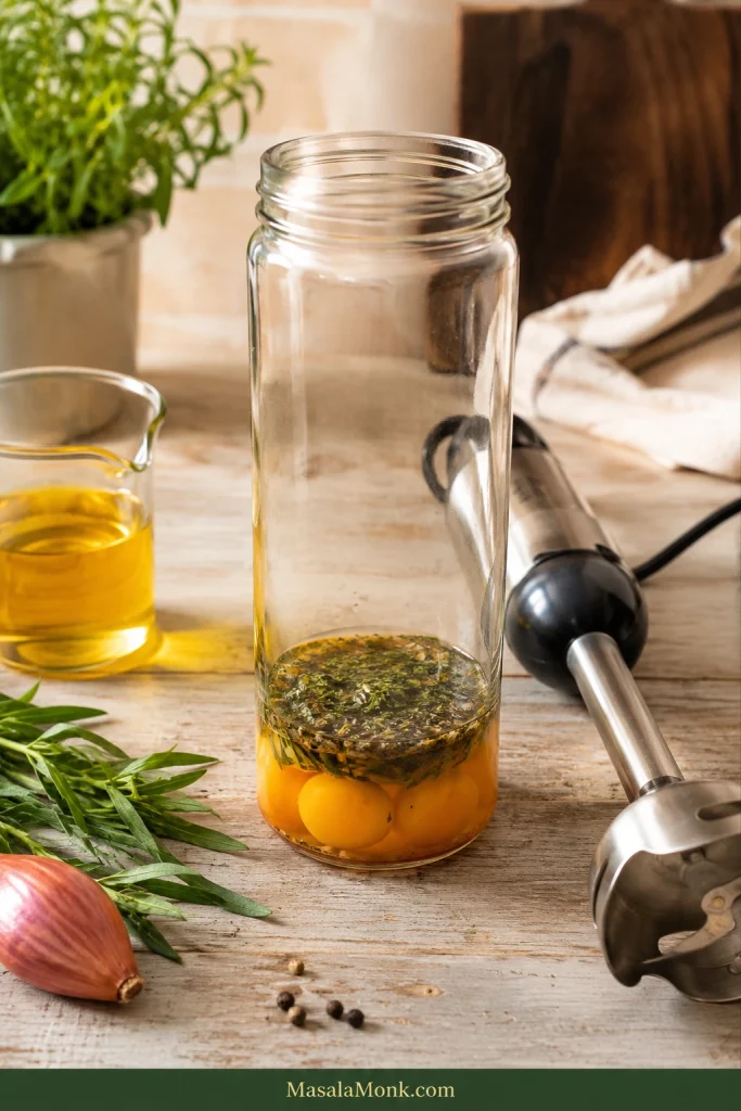 Egg yolks and strained tarragon reduction in the bottom of a tall glass blending jar before butter is added.