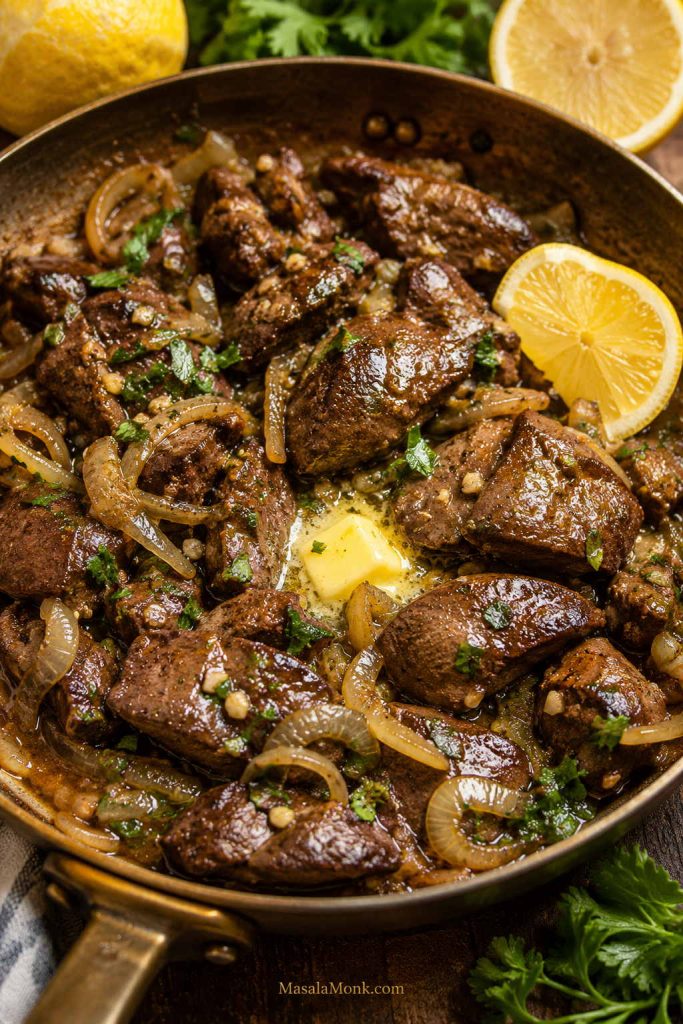 Cooked chicken livers with onions, melted butter, lemon, garlic, herbs, and glossy pan juices in a skillet.