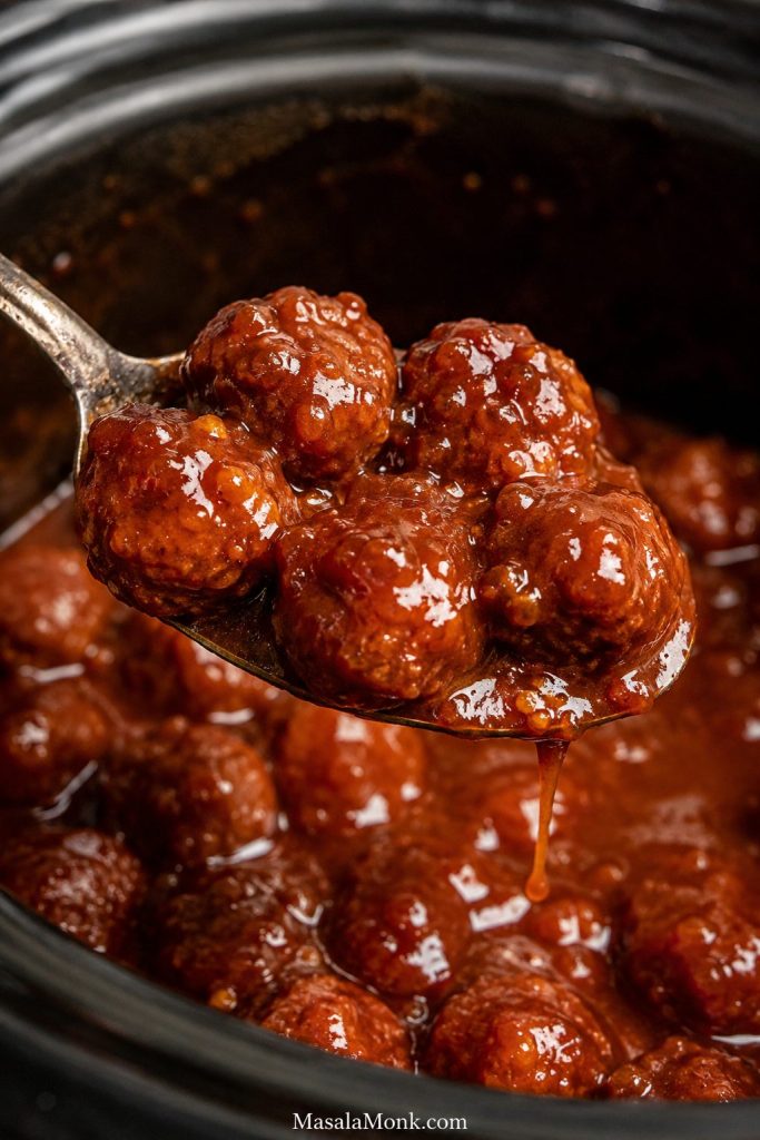 Finished grape jelly meatballs lifted on a spoon with glossy red-brown sauce clinging to them.
