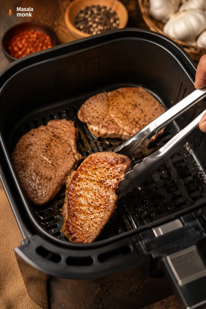 Metal tongs flipping a boneless pork chop in an air fryer basket.