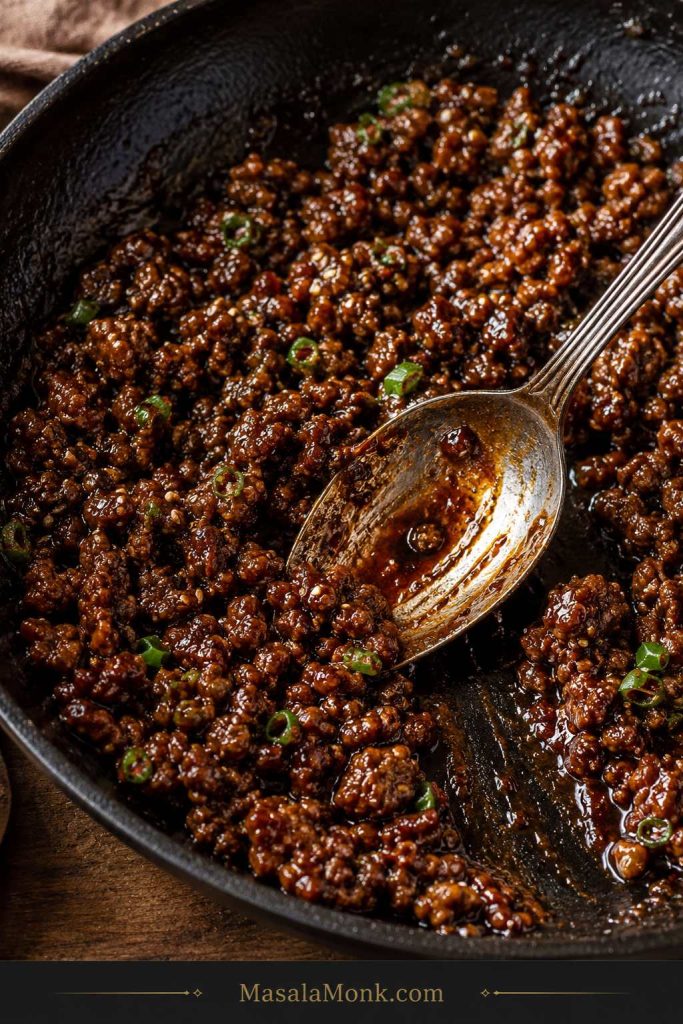 Saucy Korean-style ground beef in a dark skillet with a spoon dragged through the thickened sauce.