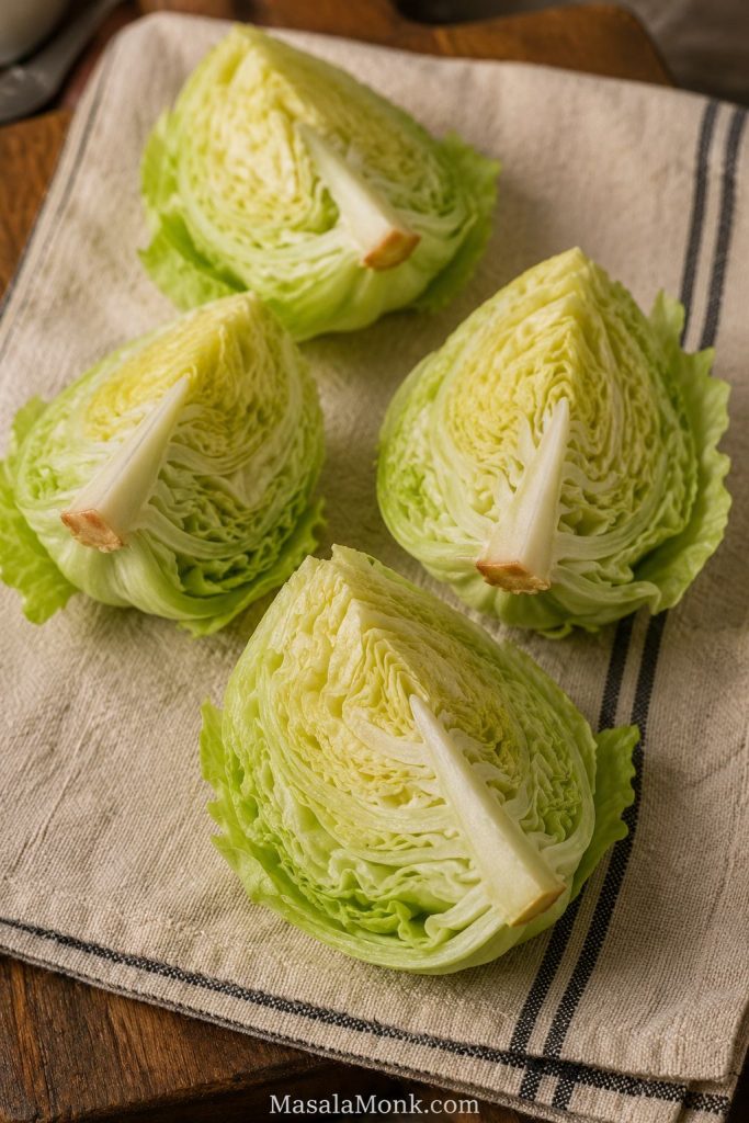Four iceberg lettuce wedges resting on a towel with a small piece of core still attached to each wedge.