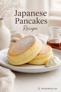 Tall Japanese soufflé pancakes stacked on a pale plate with whipped cream, powdered sugar, and syrup nearby.