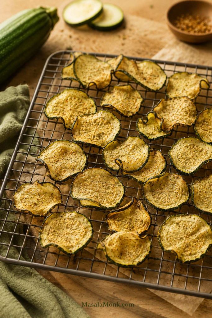 Thin lightly curled zucchini chips cooling on a wire rack.