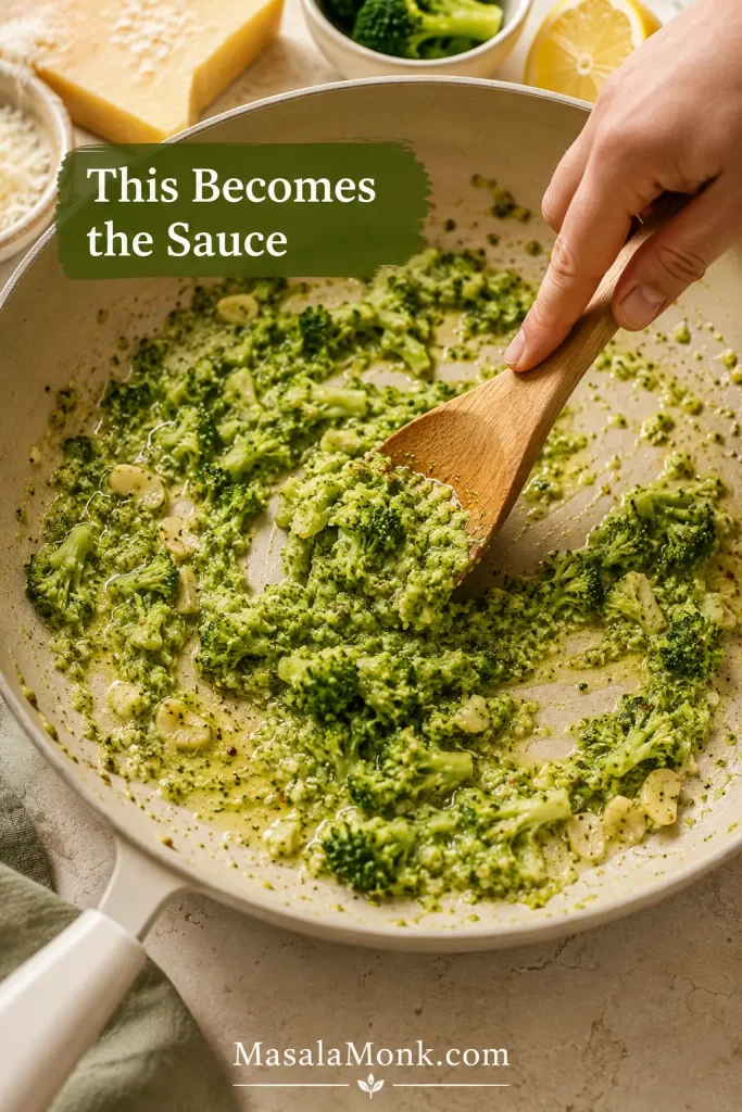 Soft broccoli being mashed with a wooden spoon in a skillet with garlic oil and butter, with text reading “This Becomes the Sauce.”