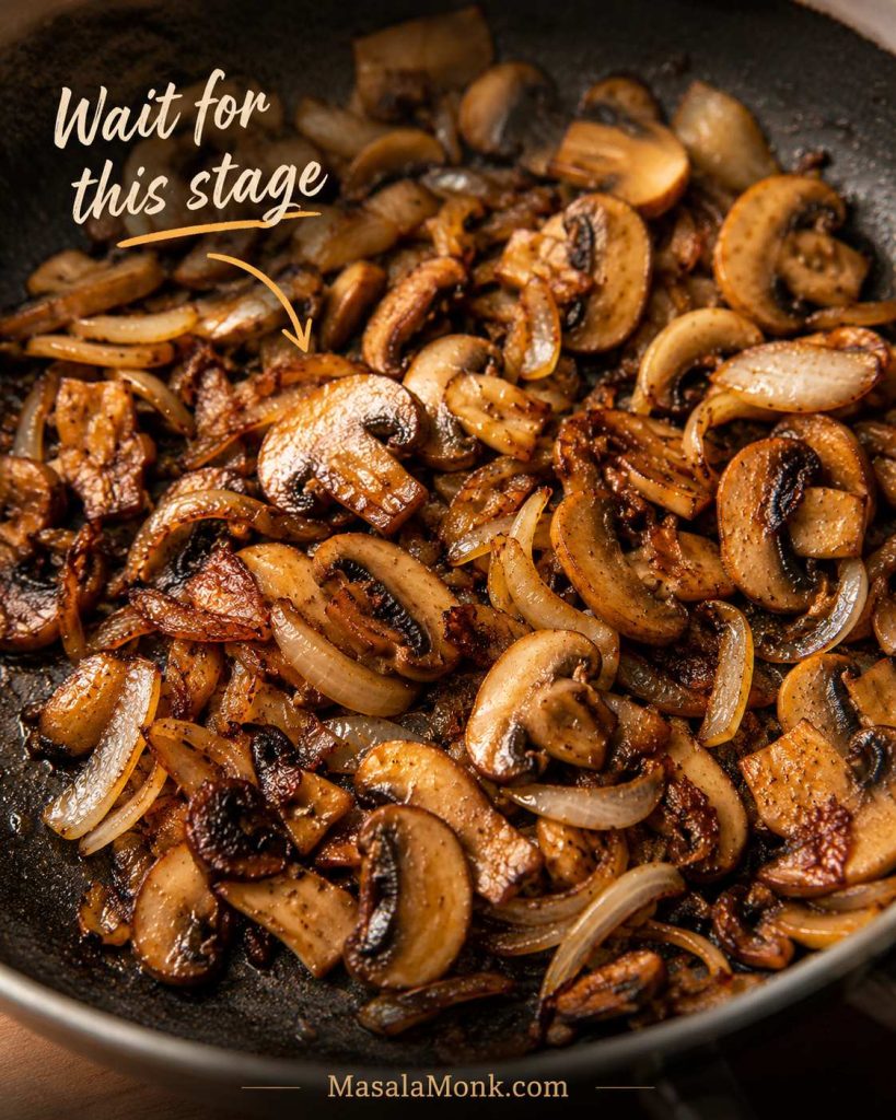 Sliced mushrooms and onions browned in a skillet with caramelized edges and the text wait for this stage.