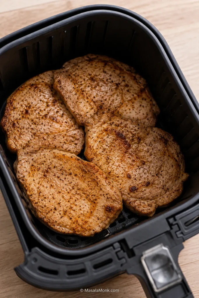 Boneless pork chops crowded and overlapping in an air fryer basket.