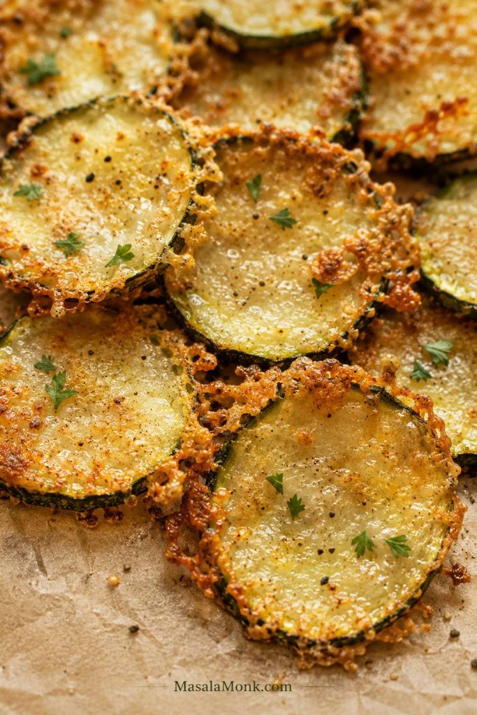 Close-up of parmesan zucchini chips with golden lacy cheese edges on parchment.