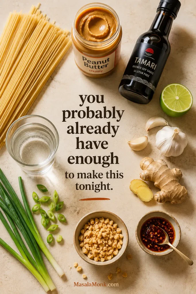Dried noodles, peanut butter, soy sauce, lime, garlic, ginger, chili, scallions, peanuts, and water arranged on a countertop