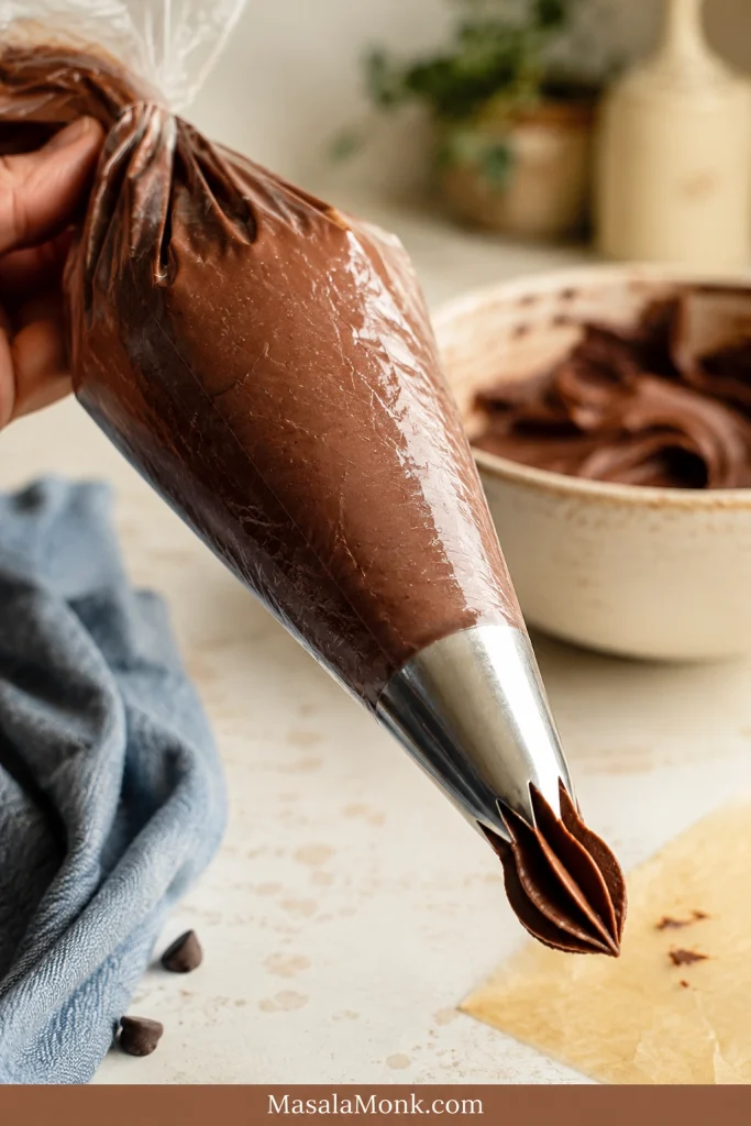 Chocolate cream cheese frosting inside a piping bag with a large star tip on a kitchen counter.