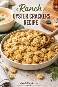 Bowl of golden ranch oyster crackers with herb flecks, scoop, and cozy snack-table sides.