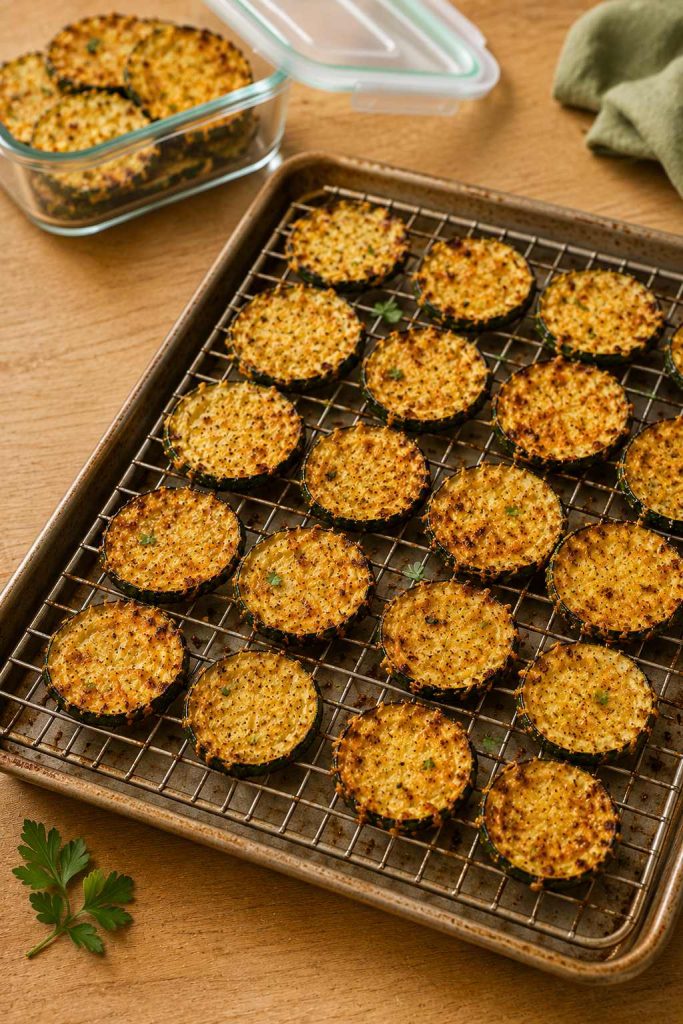 Leftover zucchini chips spread on a rack with an open storage container nearby for re-crisping.