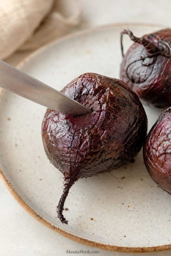 Knife inserted into the center of a roasted beet to test tenderness.