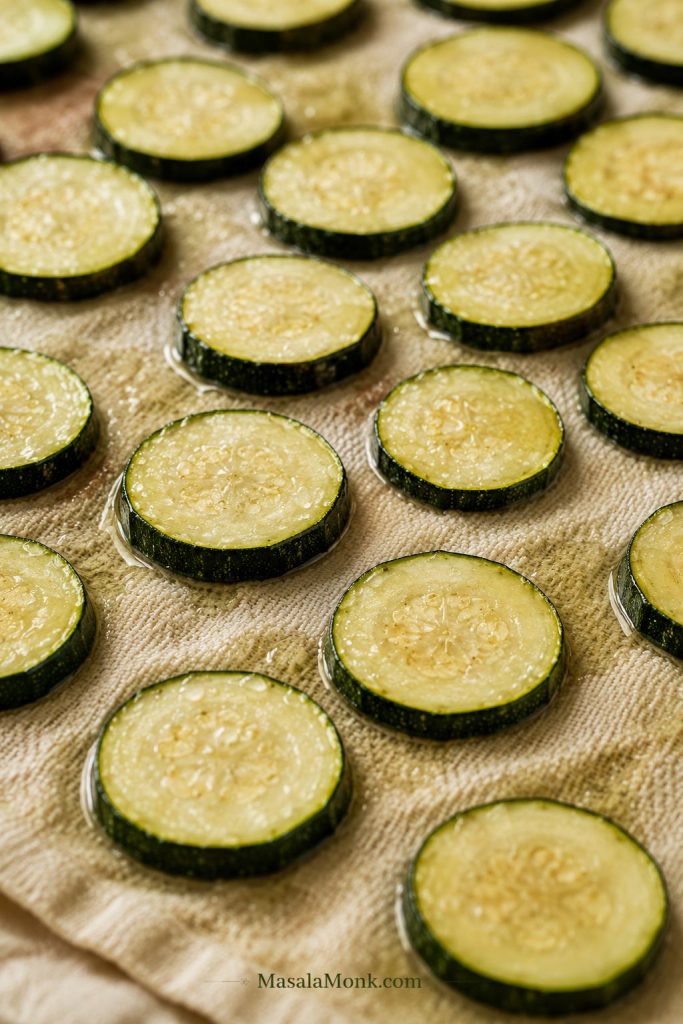 Salted zucchini rounds resting on a towel with moisture beads visible on the surface.