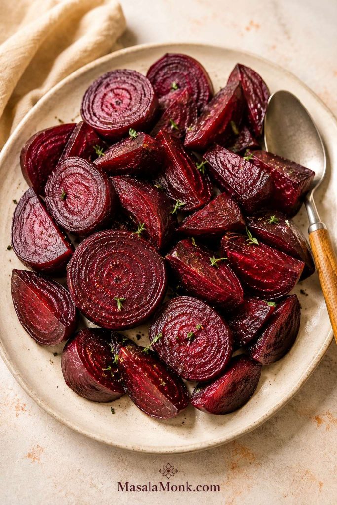 Sliced roasted beets in wedges and rounds on a cream plate with a spoon beside them.