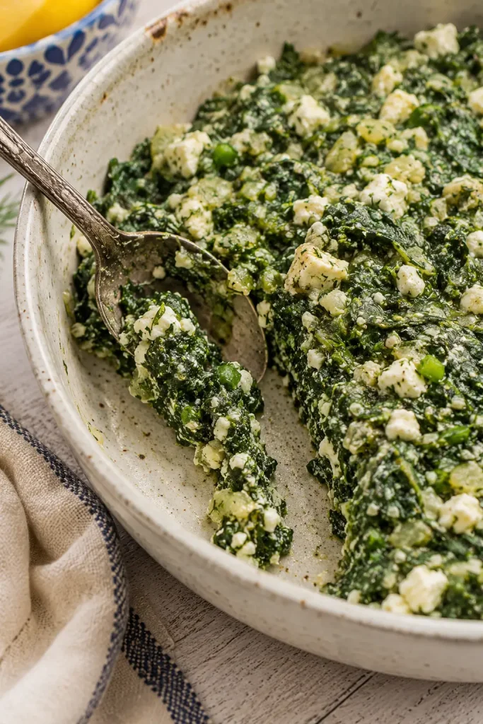 A spoon dragged through spinach and feta filling, leaving a visible trail with no liquid pooling in the bowl.