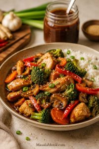 Finished chicken stir-fry with broccoli, bell peppers, carrots, mushrooms, rice, and a small jar of brown stir fry sauce in the background.