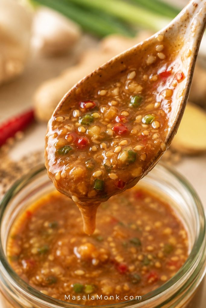 Close-up of glossy brown stir fry sauce coating a spoon, with visible bits of garlic, chili, sesame, and scallion.